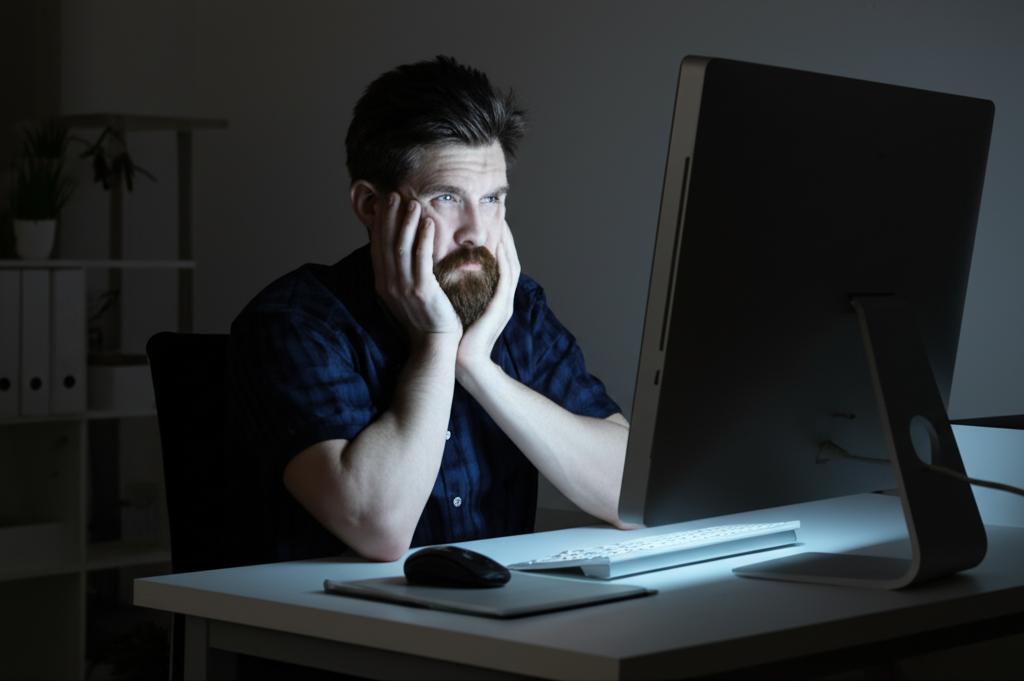 a stressed programmer sitting at his desk at night, illuminated by a computer screen, looking tired and overwhelmed, dark circles under his eyes